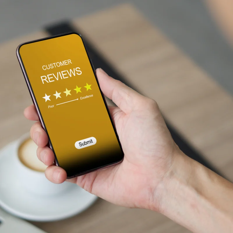 Person holding a smartphone displaying a customer review rating of five stars, emphasizing the importance of online testimonials for business credibility.